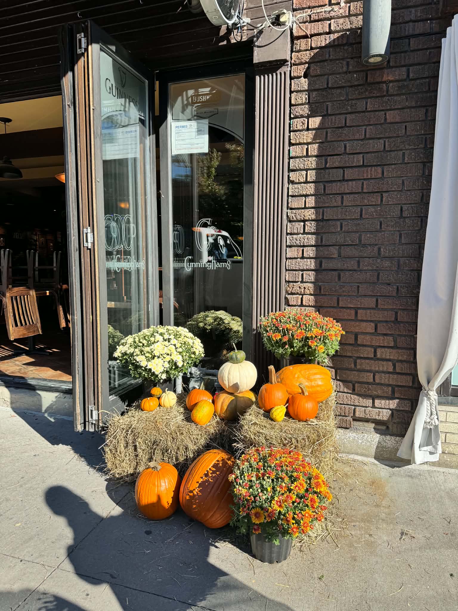 Boutique storefront autumn entrance styling with heirloom pumpkins, straw bales, and flowering planters in Pointe-Claire Village